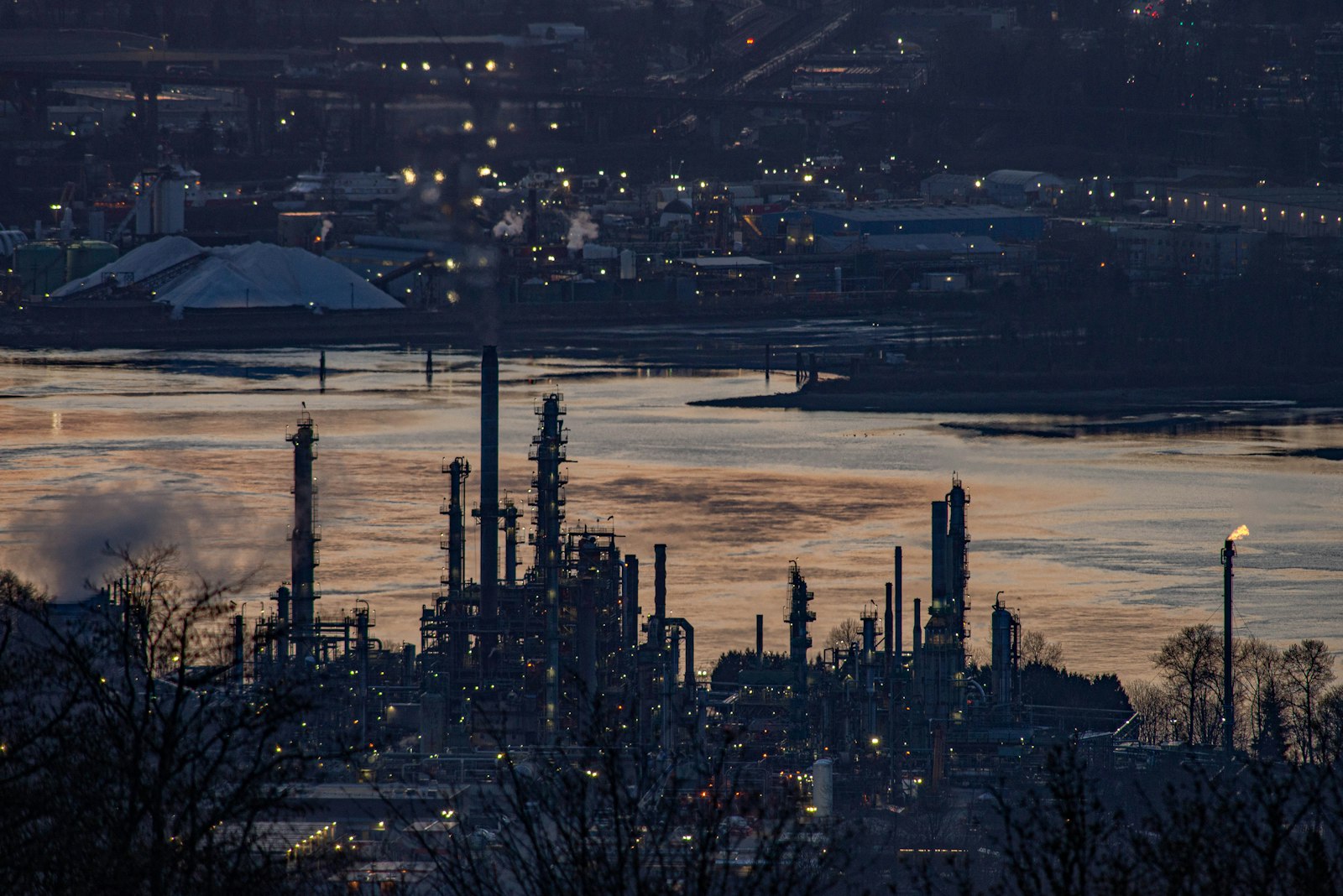 Oil refinery industrial complex with distillation columns and flare stacks at dusk