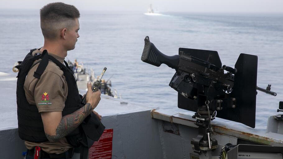 A U.S. sailor stands watch on a warship as another vessel crosses the water